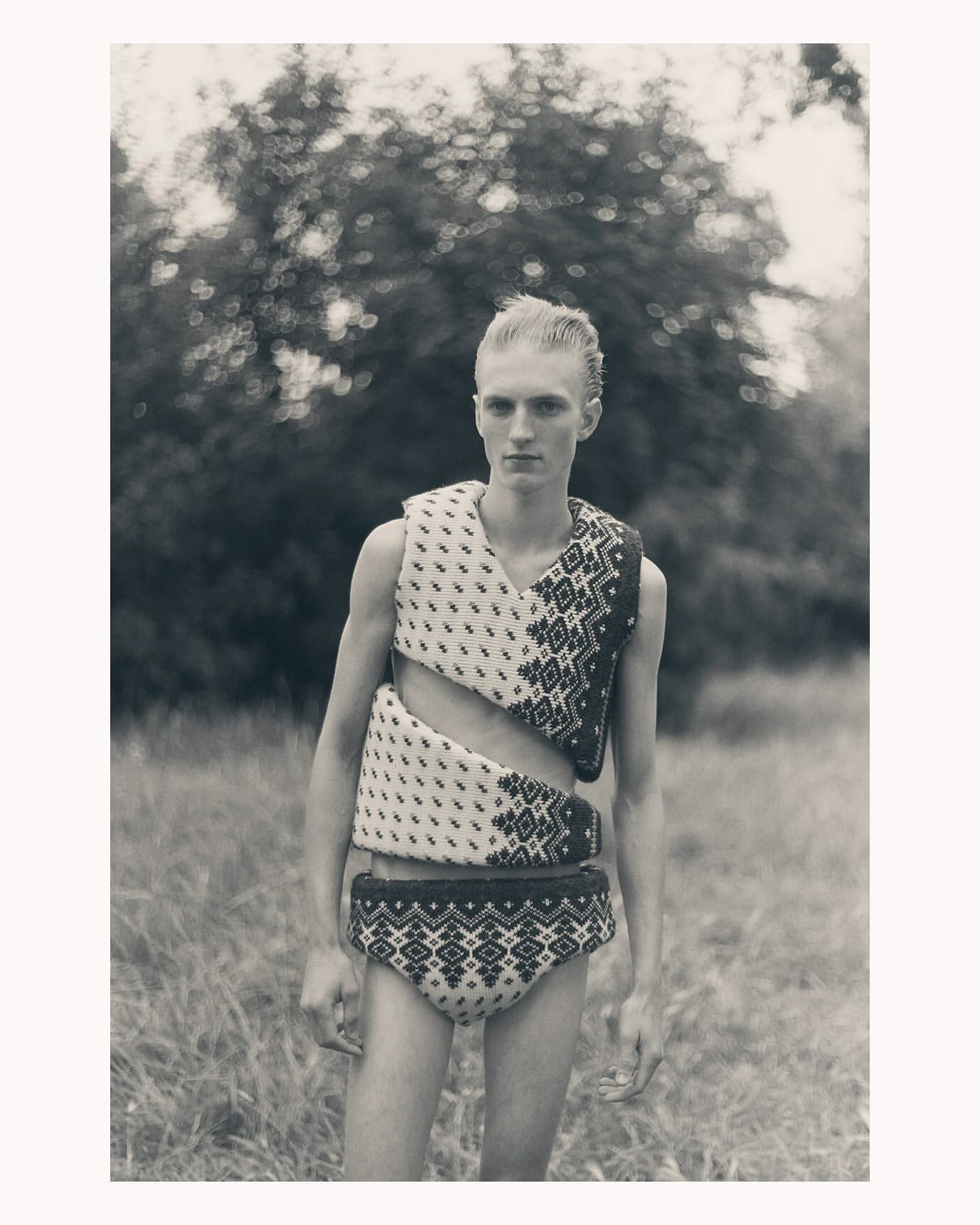 Portrait of a man wearing patterned knitted vest and shorts standing outdoors among trees captured by Ola Rindal
