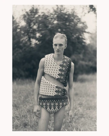 Portrait of a man wearing patterned knitted vest and shorts standing outdoors among trees captured by Ola Rindal
