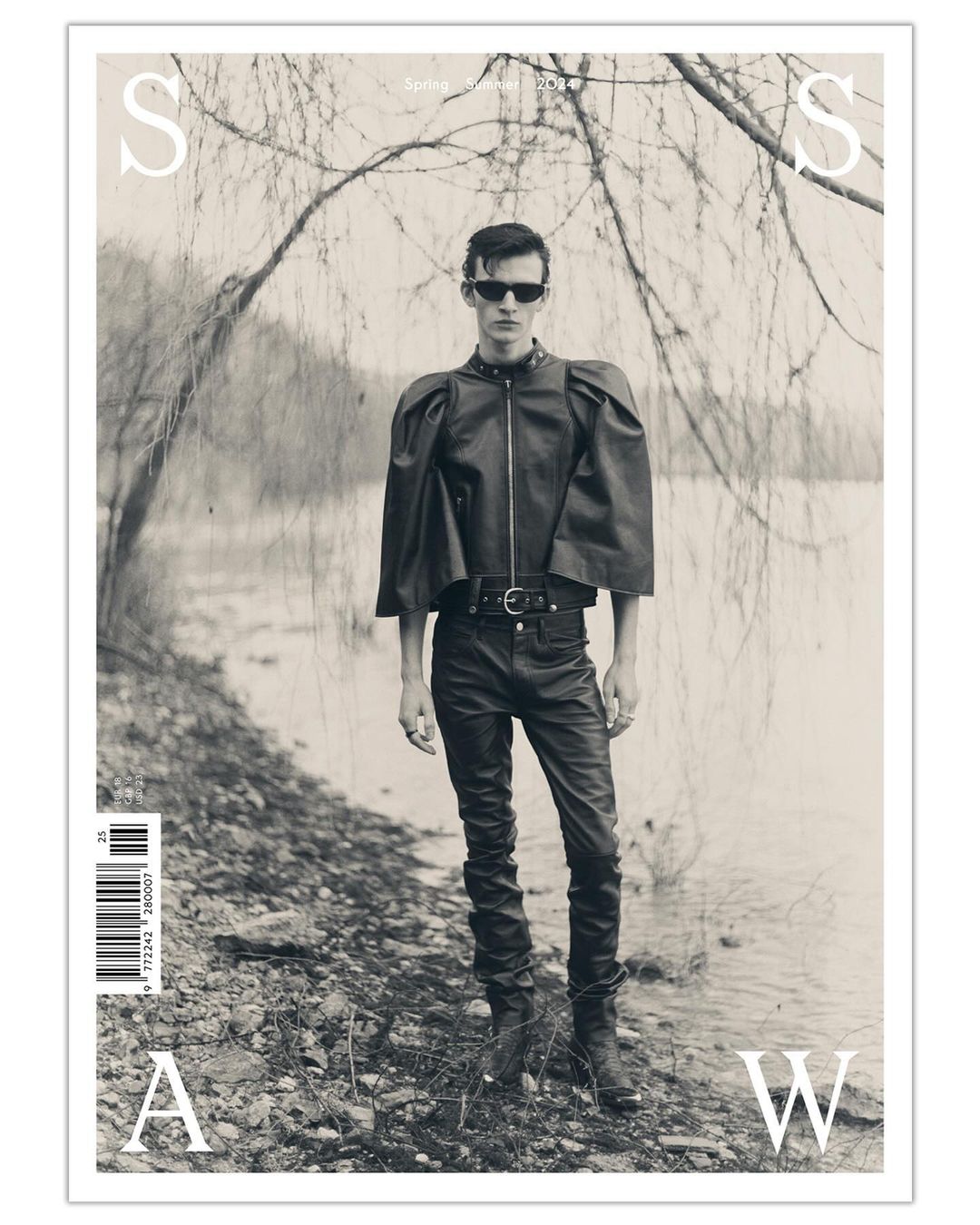 Monochrome magazine cover featuring a male model in leather clothing standing by a body of water with trees, promoting a spring/summer issue.