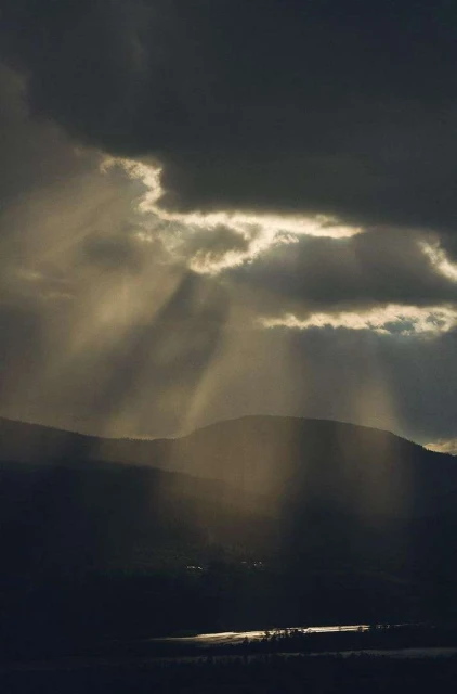 Dramatic mountain landscape with a lake reflecting sunlit rays breaking through dark storm clouds over the scene.