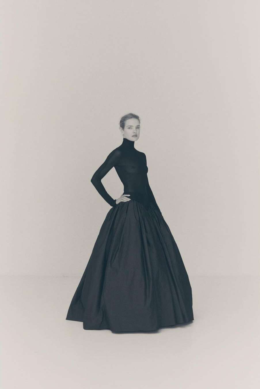 Model in a black long-sleeve turtleneck and voluminous ballgown skirt against a plain light grey studio background.
