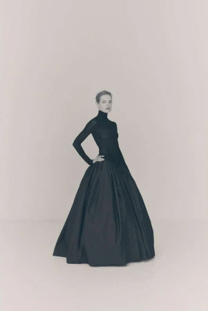 Model in a black long-sleeve turtleneck and voluminous ballgown skirt against a plain light grey studio background.