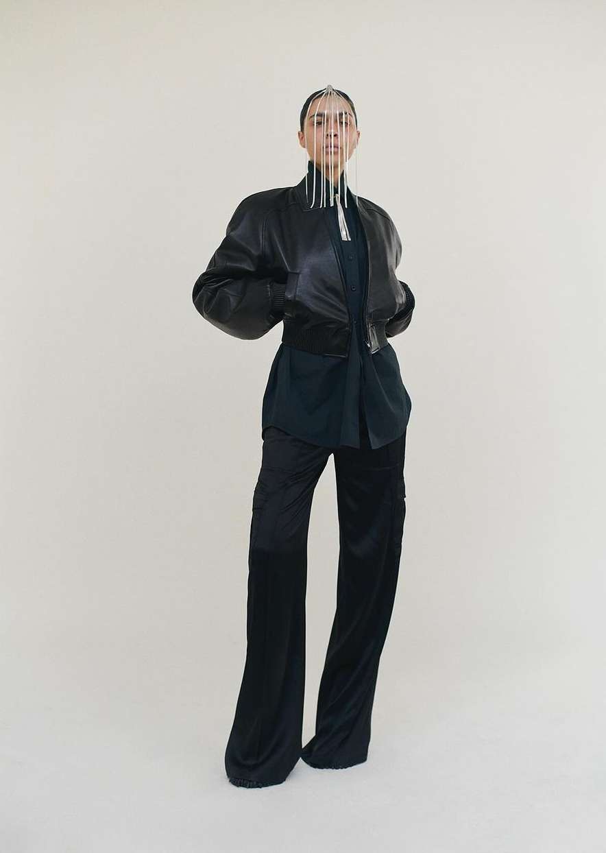 Fashion model poses in a black leather jacket and black pants with an intricate silver headpiece against a neutral backdrop.