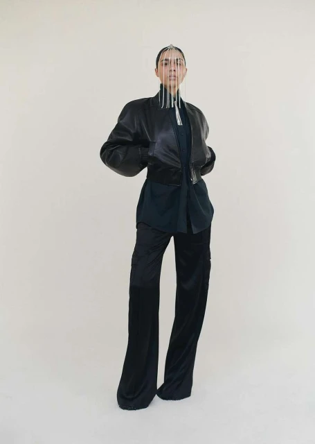 Fashion model poses in a black leather jacket and black pants with an intricate silver headpiece against a neutral backdrop.