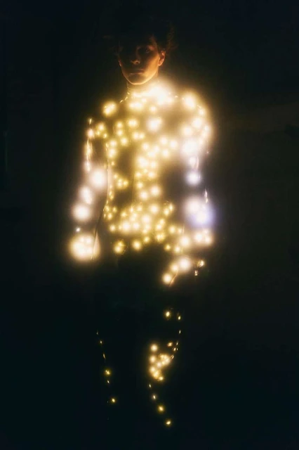 Person illuminated with string lights in a dark setting. The person's silhouette is visible against the glowing, scattered lights.