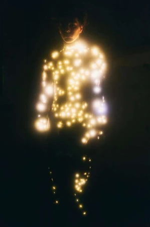 Person illuminated with string lights in a dark setting. The person's silhouette is visible against the glowing, scattered lights.