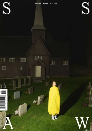 Fashion editorial featuring a model in a yellow cape, standing in a cemetery with a church in the background at nighttime.