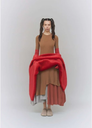 Full-length portrait of a young woman with braided pigtails wearing a brown dress and holding a large red textured scarf.