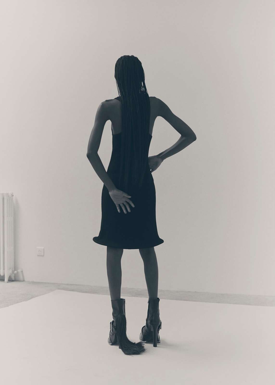 Rear view of a model in a black dress and boots standing on a white backdrop in Paris photographed by Ola Rindal.