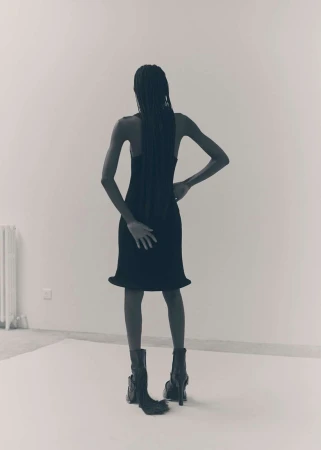 Rear view of a model in a black dress and boots standing on a white backdrop in Paris photographed by Ola Rindal.
