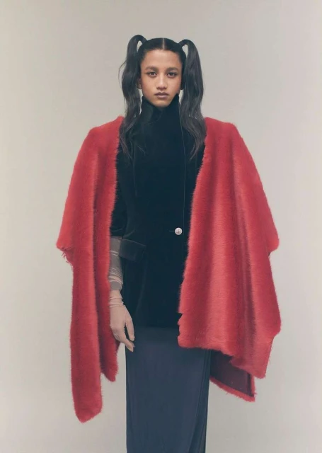 Fashion portrait of a woman with pigtails wearing a black jacket with a red shawl against a neutral background in a studio setting.
