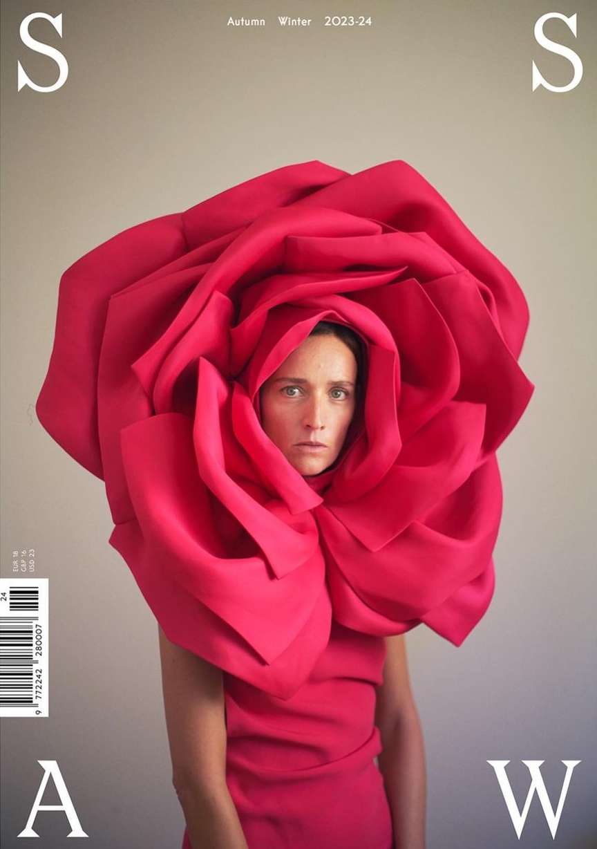 Fashion magazine cover featuring a woman in a red dress and a large rose headpiece against a neutral background.