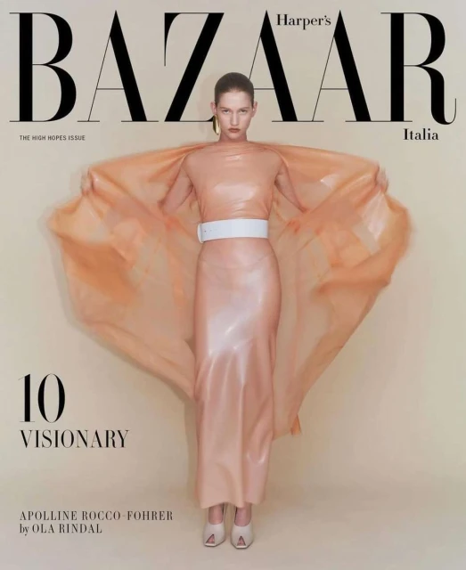 Fashion editorial photo featuring a posed model in a peach-colored dress with a white belt, posing in front of Harper's Bazaar Italia cover.