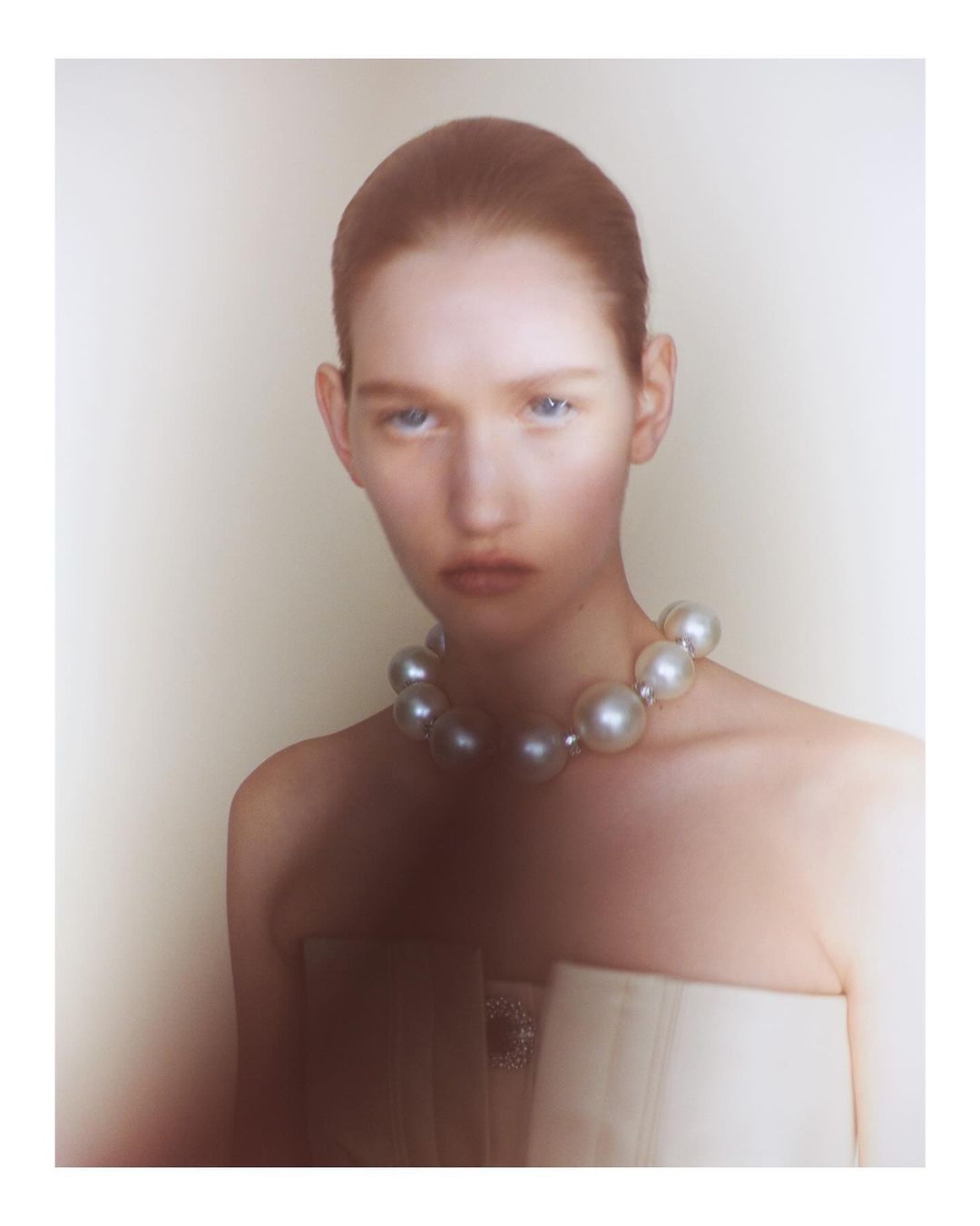 Portrait of a model wearing an oversized pearl necklace against a soft neutral background by Ola Rindal in Paris