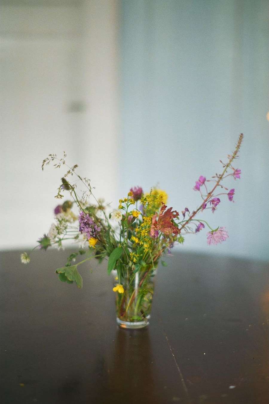 Fresh wildflower bouquet in a glass vase. Rustic table setting with natural light and delicate floral arrangement. Tabletop still life.