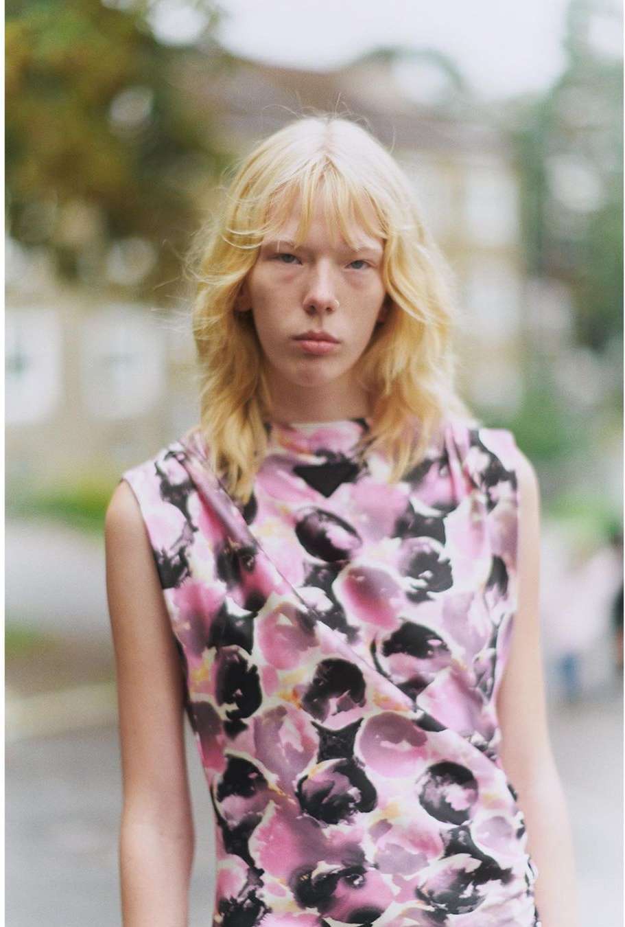 Model with long blonde hair wearing a pink and black floral sleeveless top outdoors in Paris.