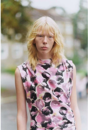 Model with long blonde hair wearing a pink and black floral sleeveless top outdoors in Paris.