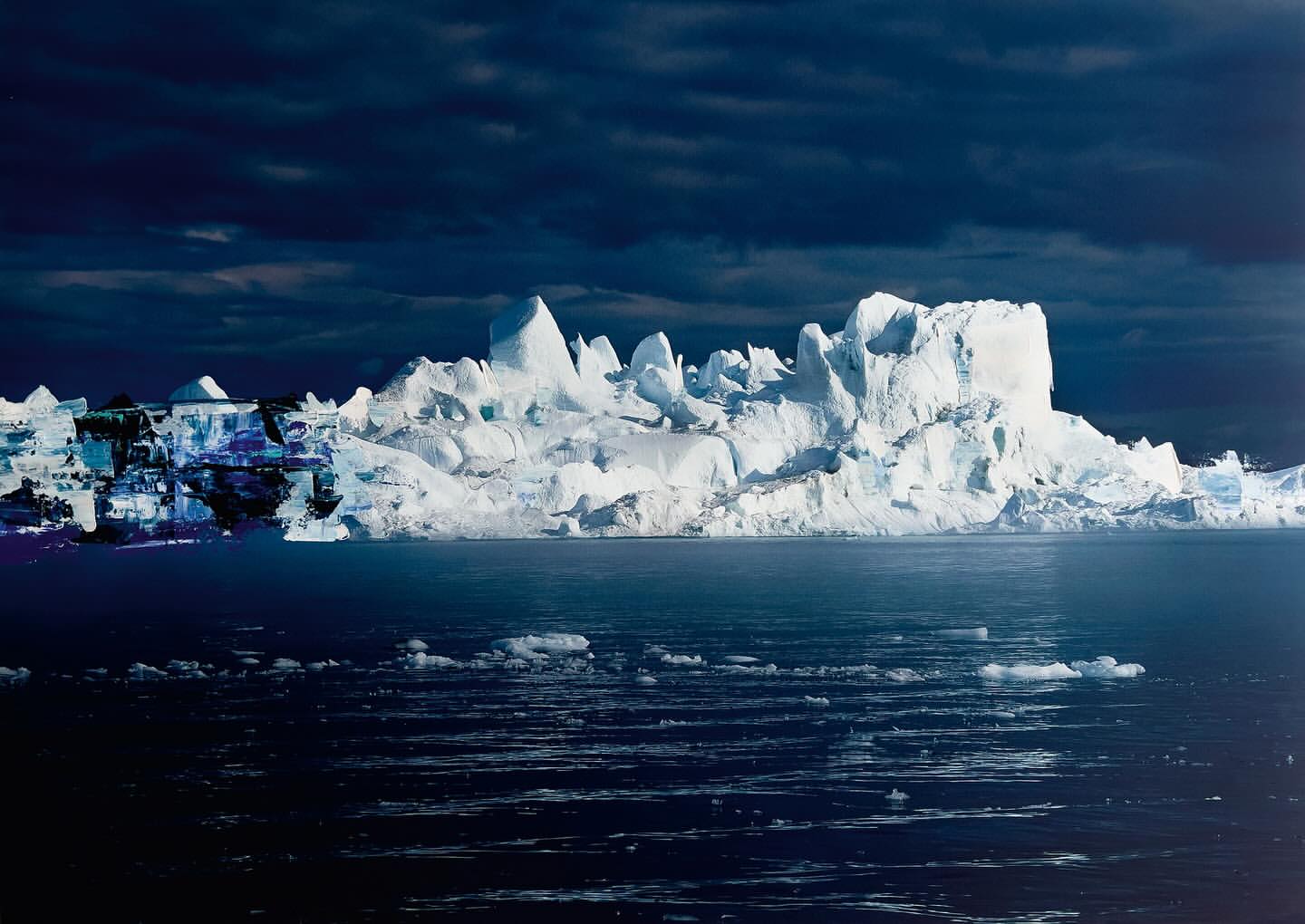 A large iceberg floats in the dark ocean under a cloudy sky, creating a dramatic and cold polar landscape.