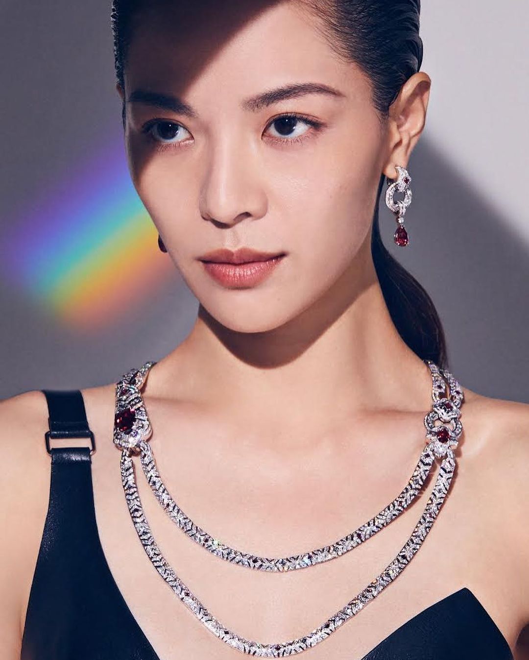 Close-up of an adult woman with a neutral expression, wearing a black top and ornate silver and ruby necklace and matching earrings.