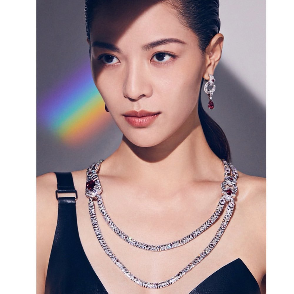 Close-up of an Asian woman with a ponytail, wearing a black top, ornate silver necklace, and earrings, with a rainbow light effect.