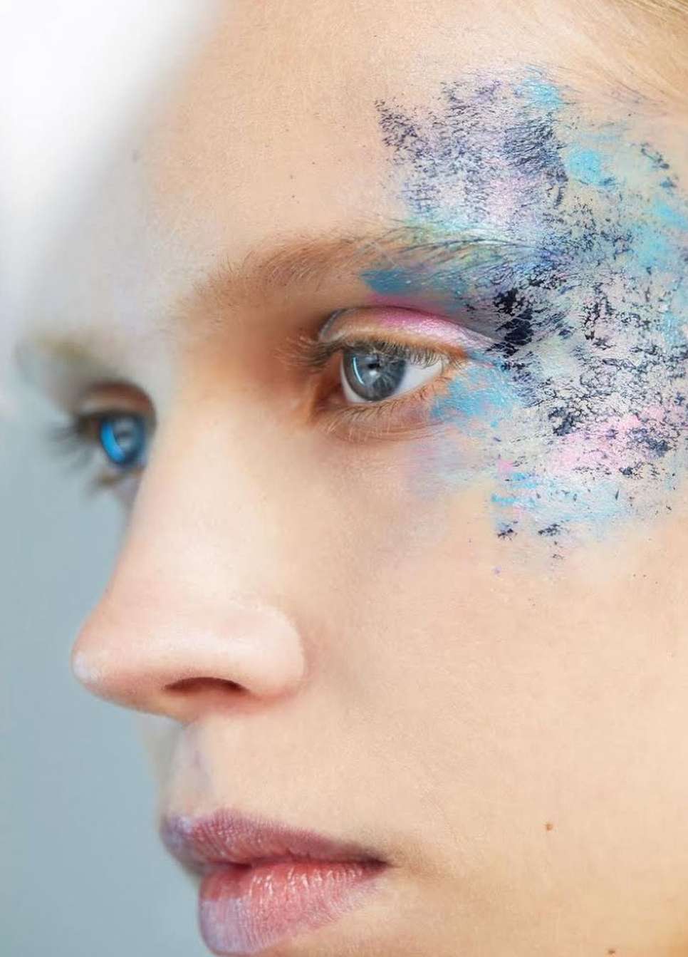 Close-up portrait of an adult female with striking blue eyes and decorative makeup applied around her eye and temple. Beauty concept.