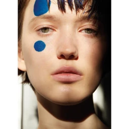 Close-up portrait of a woman with blue painted dots on her forehead and cheek photographed by Olaf Wipperfurth in Paris.