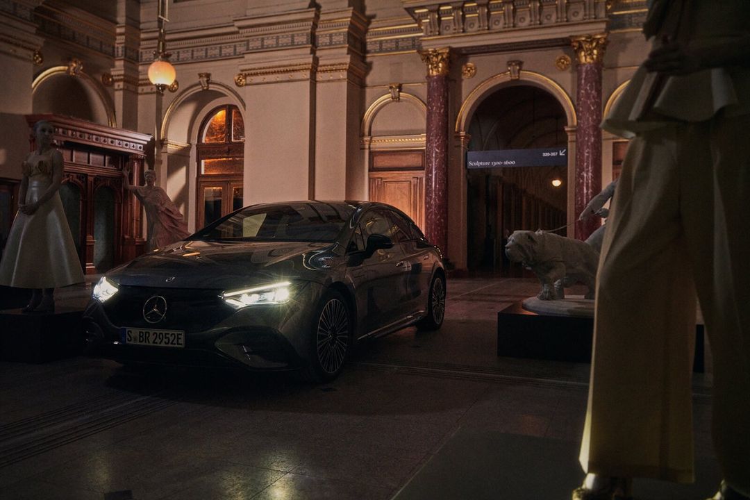 Sleek black Mercedes-Benz EQE parked indoors; elegant architectural details & artful presentation create an upscale, sophisticated ambiance.
