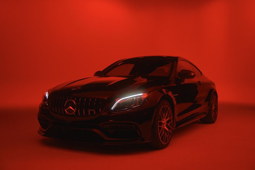 Sleek black Mercedes-AMG C 63 Coupe showcased in a photo studio with vibrant red lighting highlighting its sporty design.