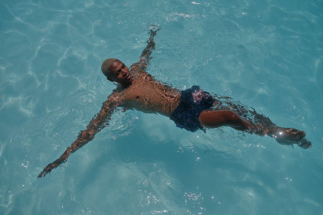 A person floats on their back in a pool of clear turquoise water with arms outstretched on a sunny day.