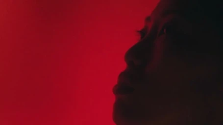 Close-up profile of a woman looking upward bathed in dramatic crimson red lighting