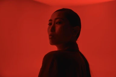 Portrait of a woman with dark hair looking over her shoulder against an intense red monochromatic background.