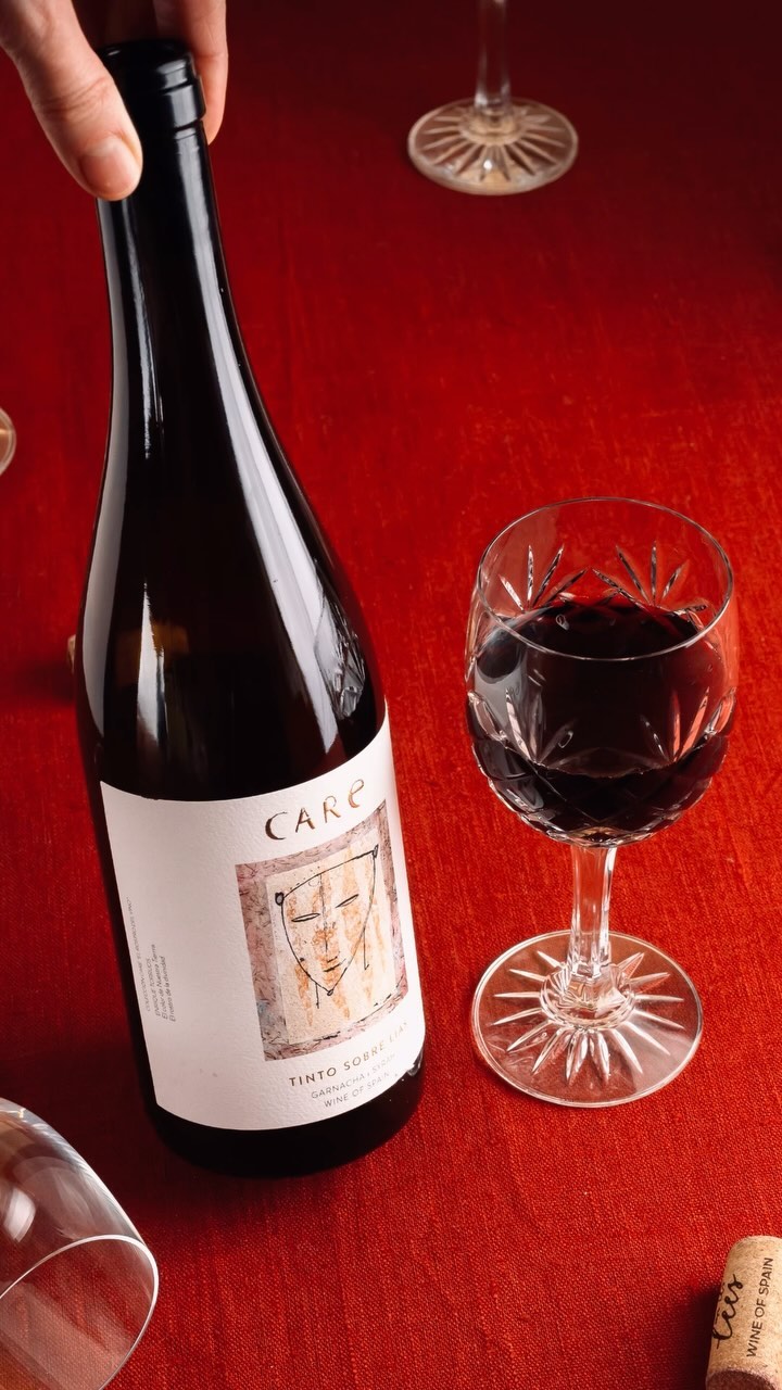 Still life of a bottle of red wine and a wine glass on a red tablecloth, showcasing the dark wine and elegant glassware.