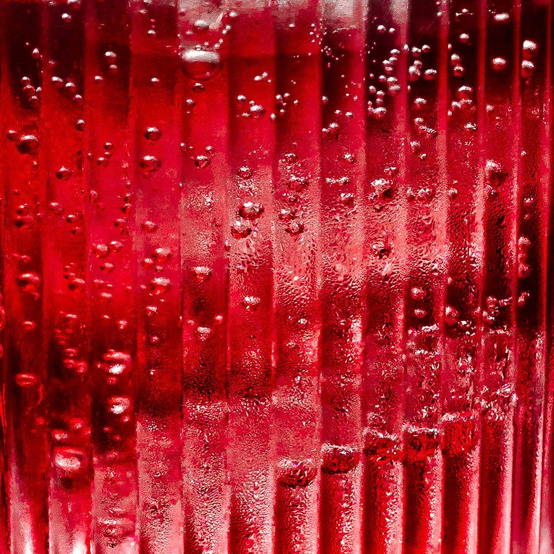 Close-up of a vibrant red beverage with a bubbly texture inside a ridged glass, creating an abstract and refreshing visual.