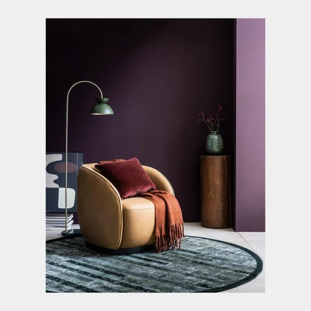 Interior design featuring a beige armchair with maroon pillow and throw, a green floor lamp, and a deep purple wall.