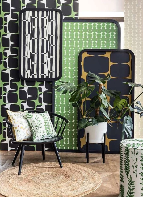 Interior with black spindle chair, round jute rug, a potted plant, and framed graphic pattern panels in green, black, and white.
