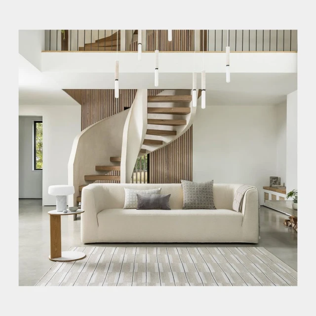Contemporary living room showcasing a modern cream-colored sofa, patterned rug, and unique staircase, illuminated by modern hanging lights.