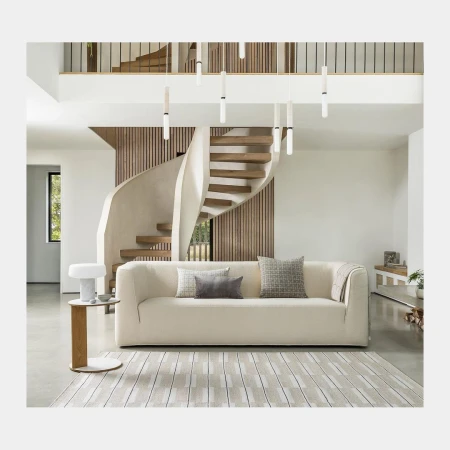 Contemporary living room showcasing a modern cream-colored sofa, patterned rug, and unique staircase, illuminated by modern hanging lights.