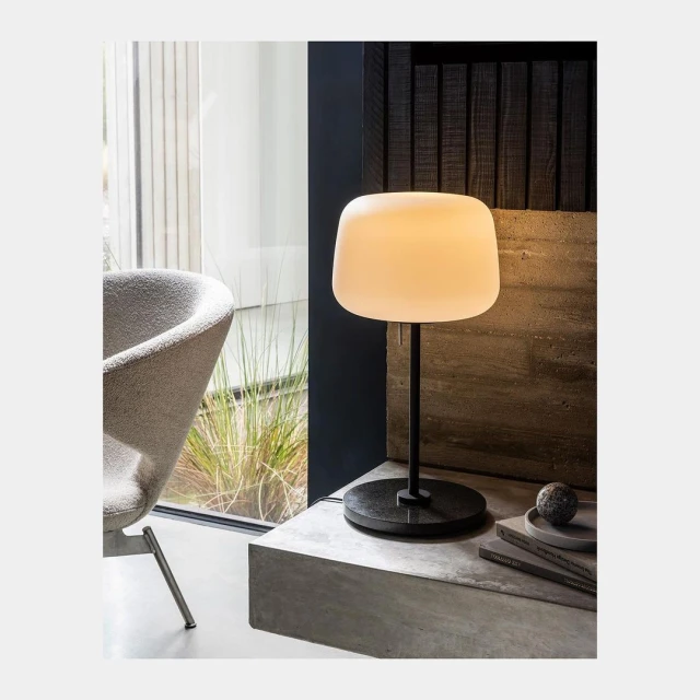 Contemporary interior shot featuring a glowing table lamp with a light-beige shade and dark base, complemented by modern furniture.