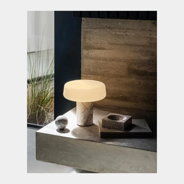 Illuminated mushroom-style table lamp with marble base on concrete surface, accompanied by a small decorative ball and dish.