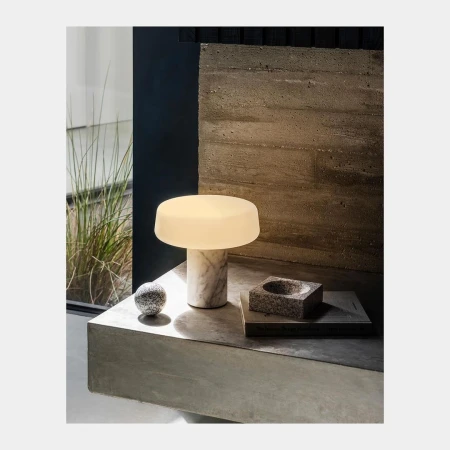 Illuminated mushroom-style table lamp with marble base on concrete surface, accompanied by a small decorative ball and dish.