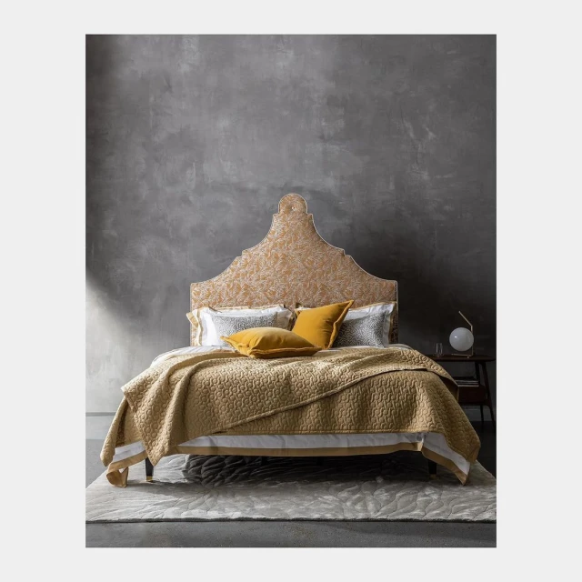 Bedroom with a decorative headboard, yellow quilt, pillows, and a gray textured wall in the background creates a cozy aesthetic.