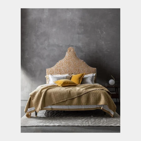Bedroom with a decorative headboard, yellow quilt, pillows, and a gray textured wall in the background creates a cozy aesthetic.