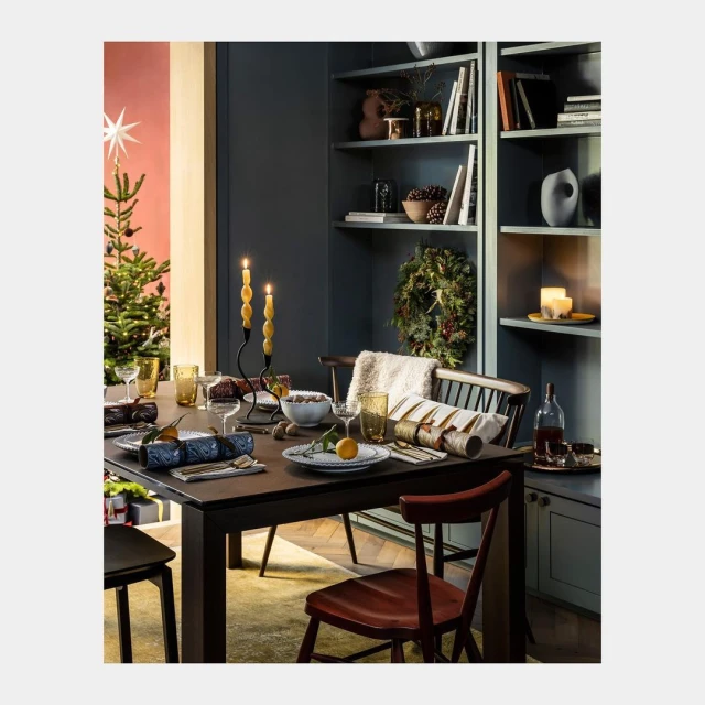 Christmas table setting with crackers, candles, wine, and a Christmas tree in the background. Festive holiday dining decor.