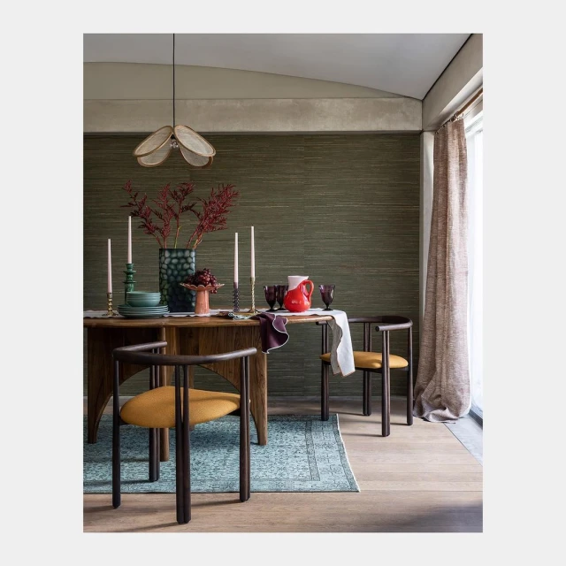 Dining room interior: a wooden table set with candles, glassware, and a vase of red foliage. Dark wood chairs, natural light.