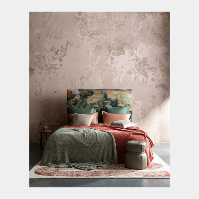 Bedroom interior featuring a bed with a patterned headboard and several pillows, set against a textured wall, with warm lighting.