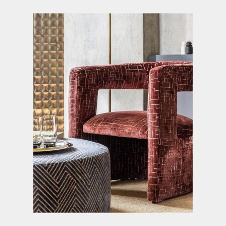 Upholstered armchair with modern geometric patterns next to a round ottoman with a glass and metal tray holding two glasses.
