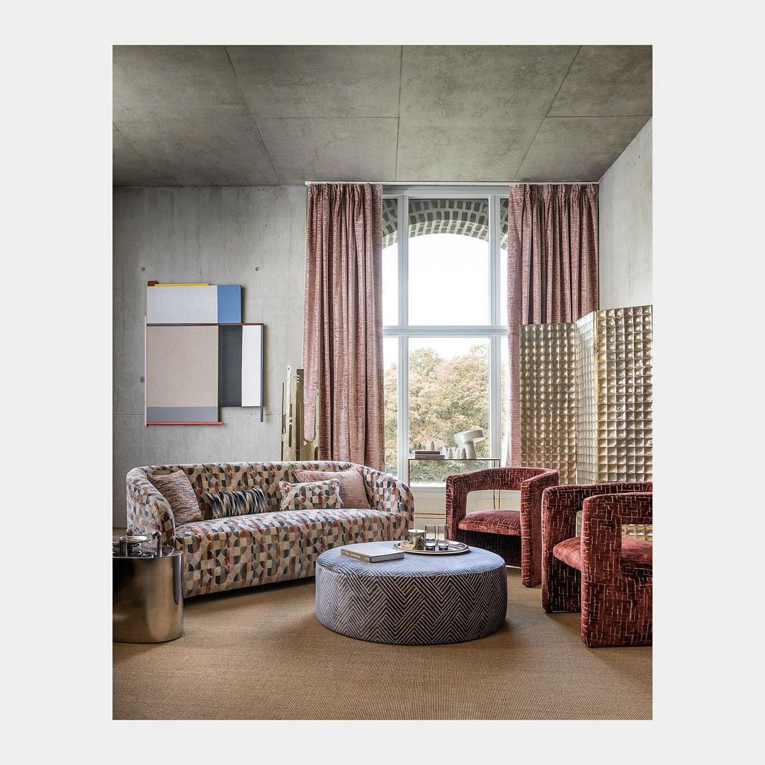 Modern interior living room with patterned sofa, round ottoman, and large arched window with patterned curtains.