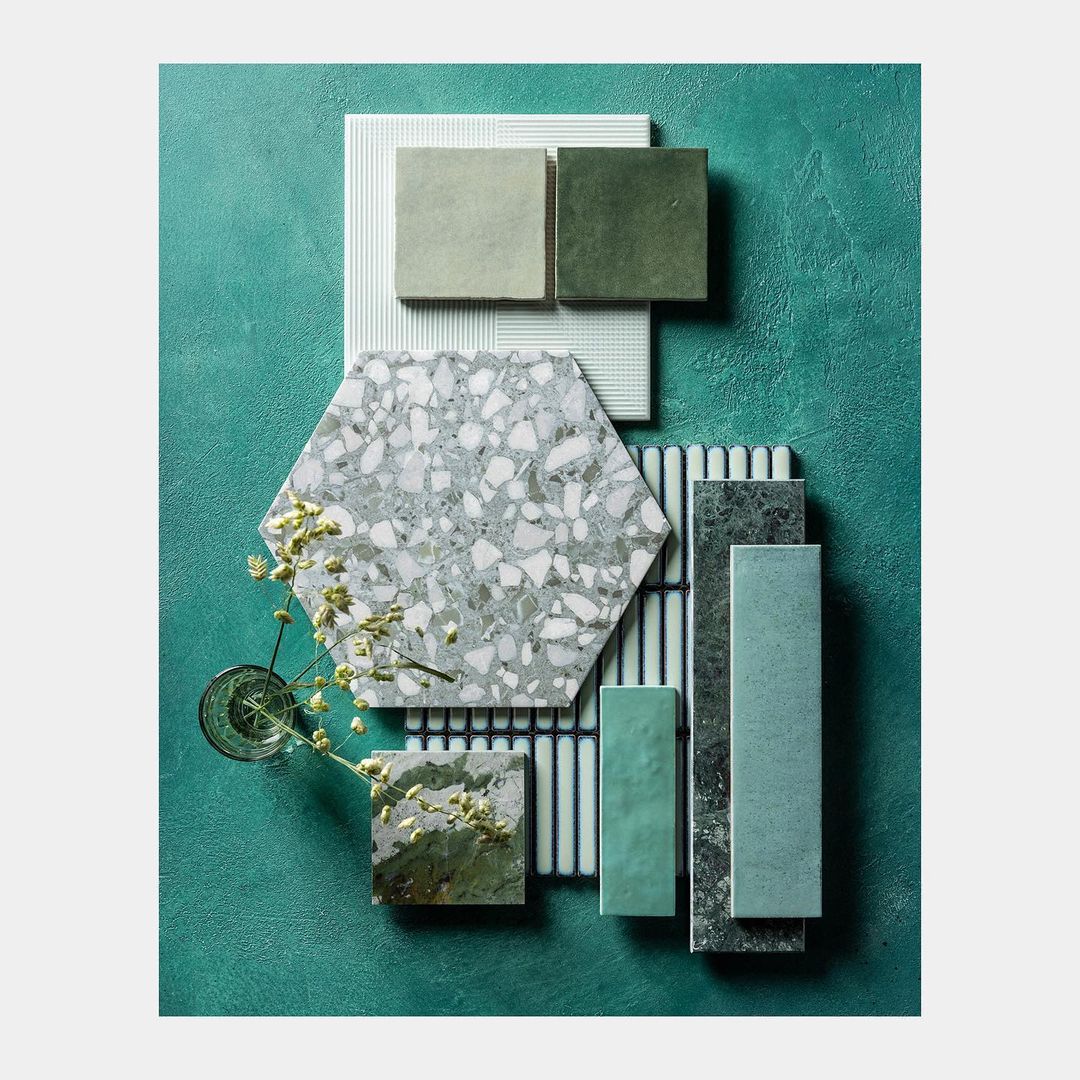 Still life of assorted geometric tile samples in various shades of green, blue, and gray, arranged on a textured teal background.