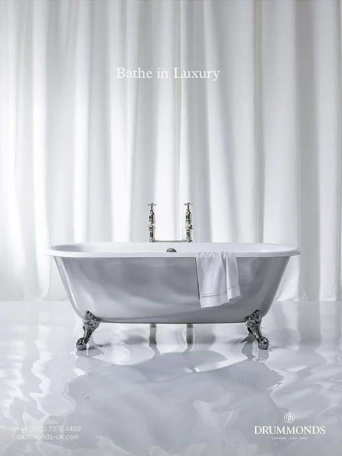 Elegant clawfoot bathtub with silver finish and chrome fixtures, complemented by a white towel and sheer white curtains.