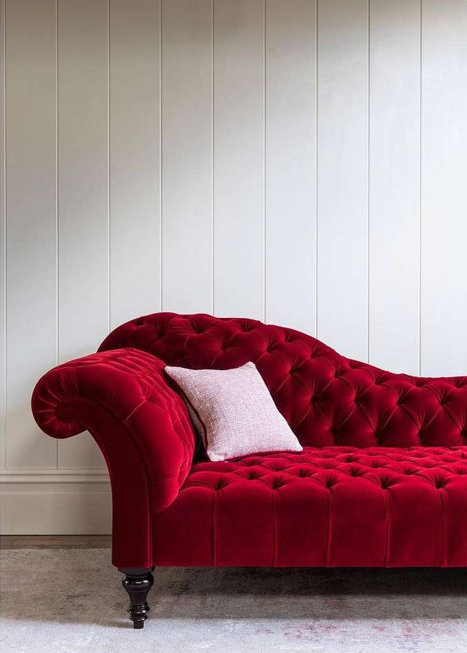 Elegant chaise lounge upholstered in deep red velvet with tufted cushions, complemented by a soft cushion, set against a paneled wall.